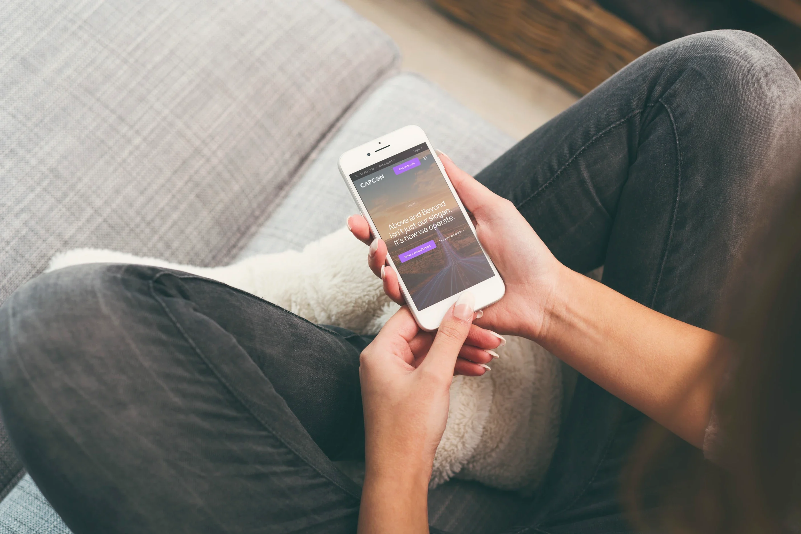 The About page on a phone held on a sofa: 'Above and Beyond isn't just our slogan. It's how we operate.'