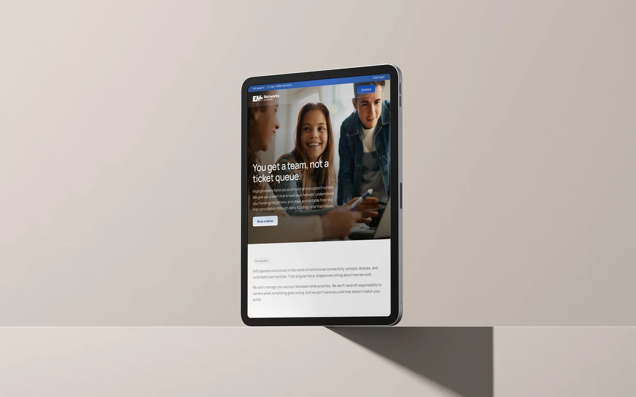 The Why EM3 page on a tablet standing on a shelf: 'You get a team, not a ticket queue.'