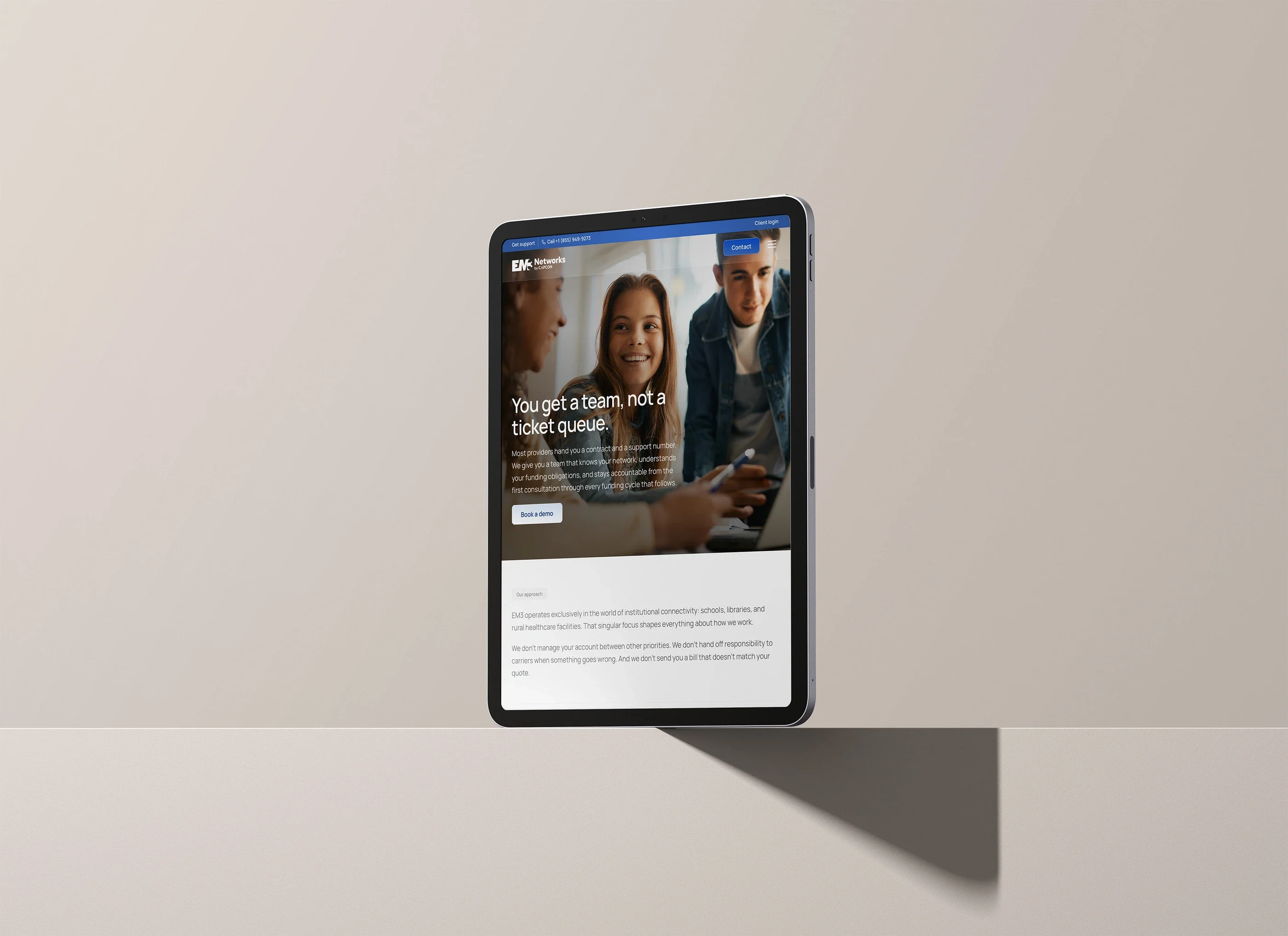 The Why EM3 page on a tablet standing on a shelf: 'You get a team, not a ticket queue.'