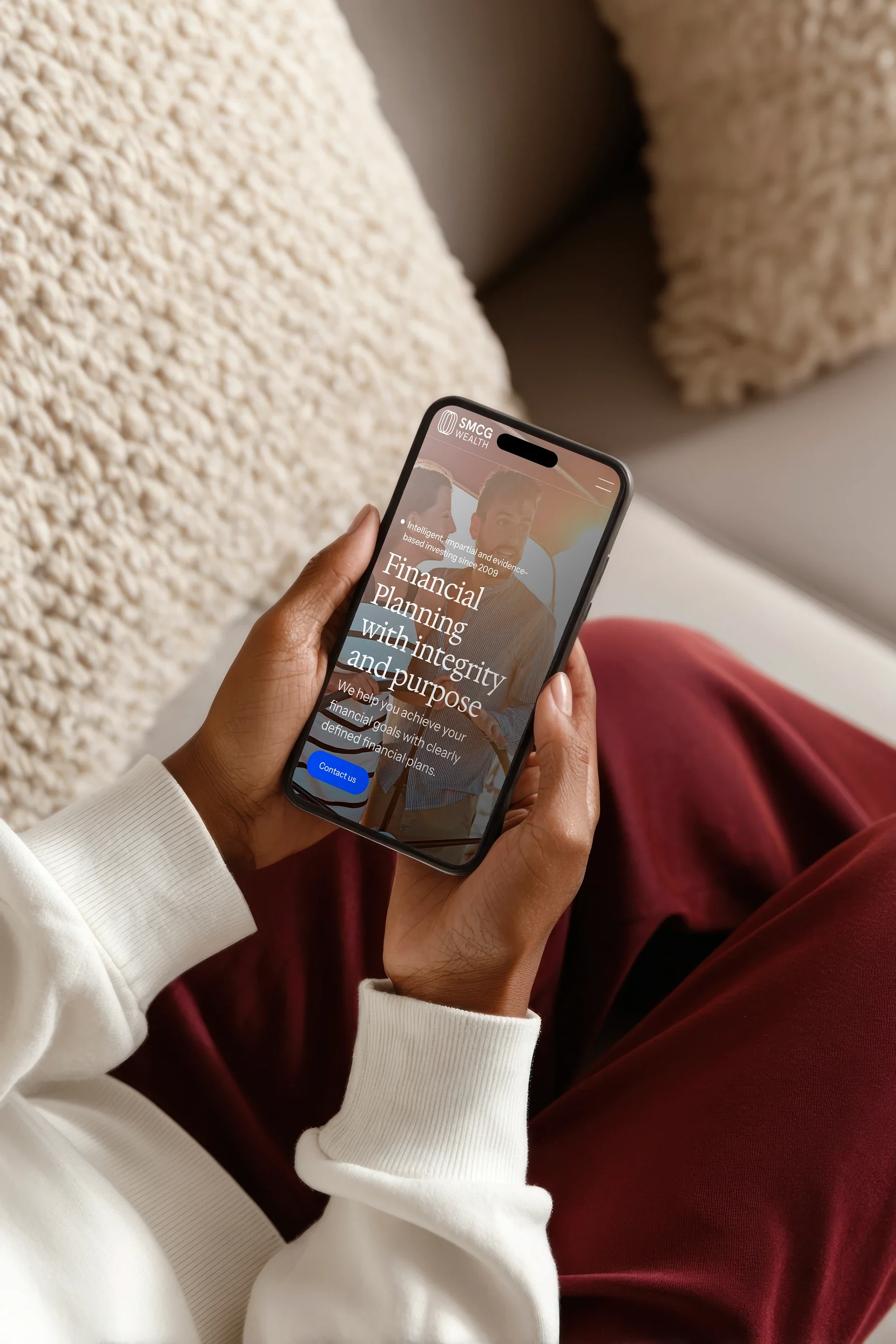 The SMCG Wealth home page on a phone held in someone's lap: 'Financial Planning with integrity and purpose'