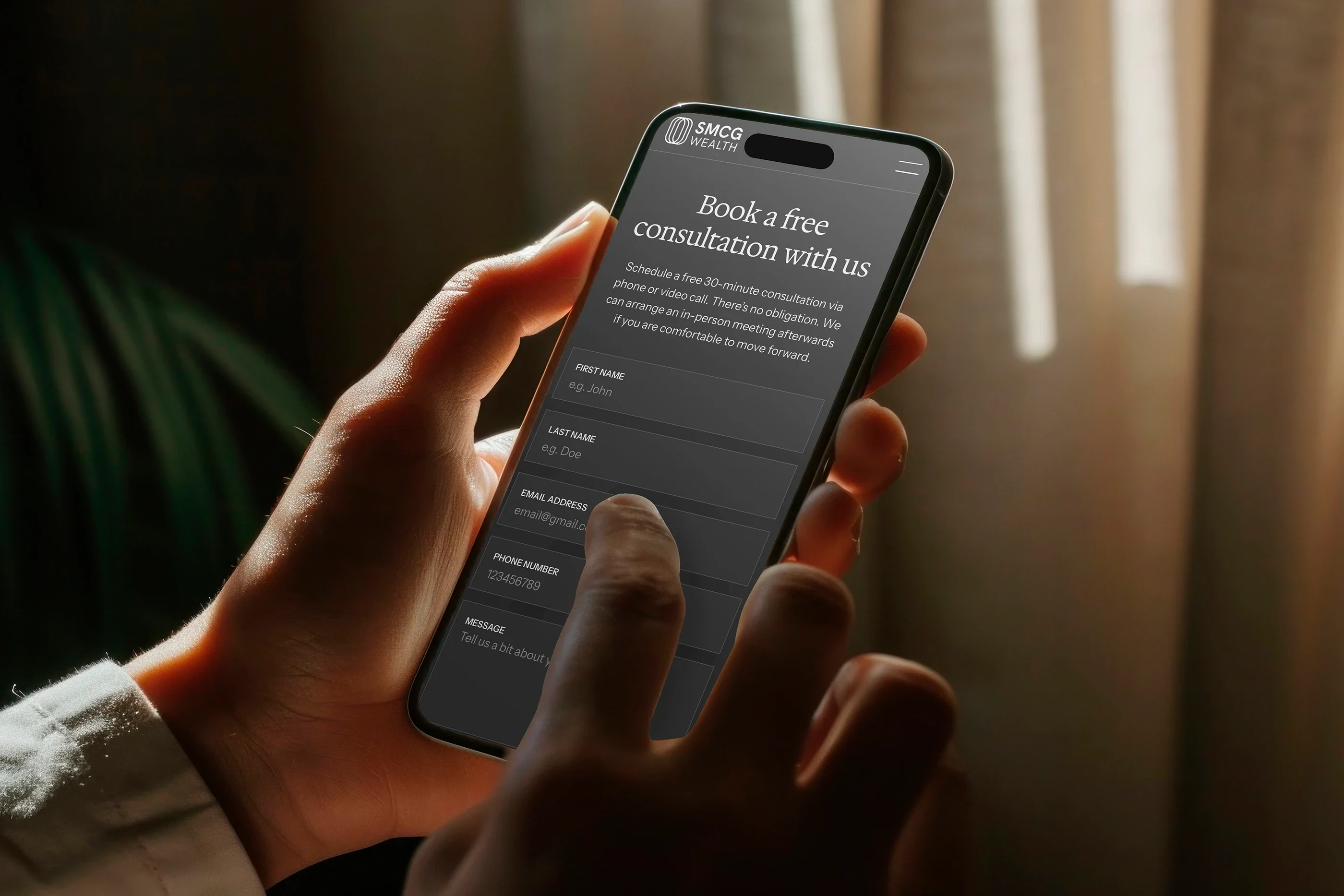 The contact page on a phone held in warm light: 'Book a free consultation with us'
